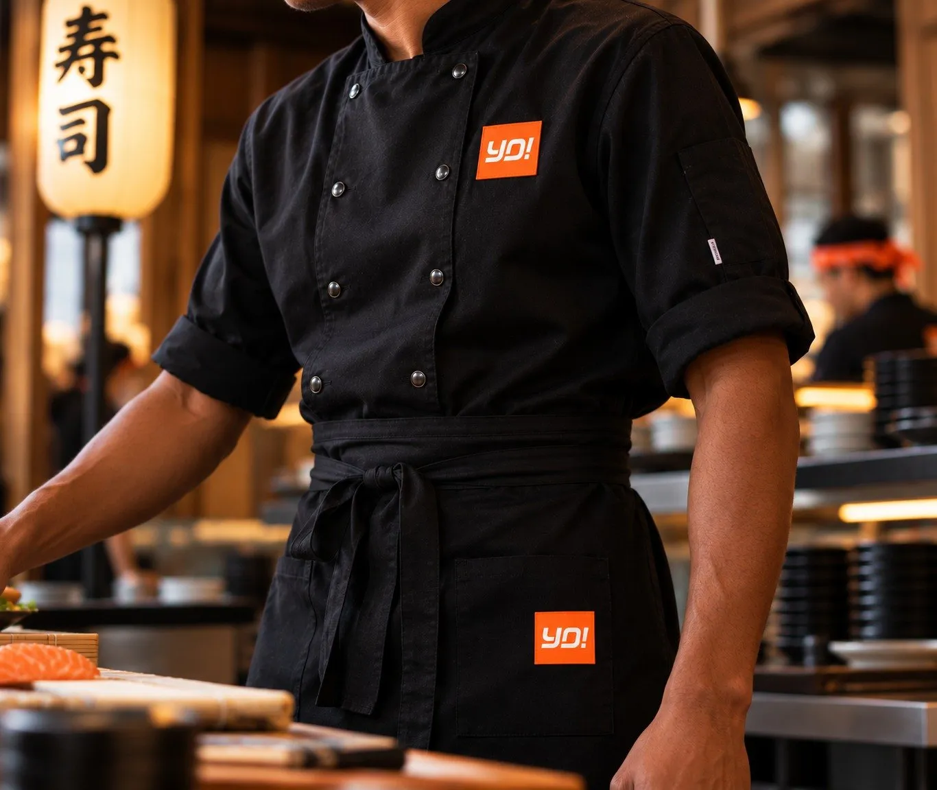 YO! chef in a branded black chef jacket and apron at the sushi counter